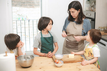 Mother giving baking instructions to her three children in a bright kitchen