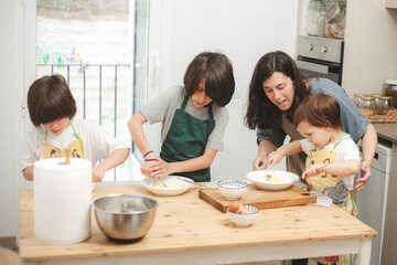 Children mixing cookie ingredients with mother's supervision in kitchen