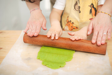 Mother and toddler flattening green dough together with rolling pin