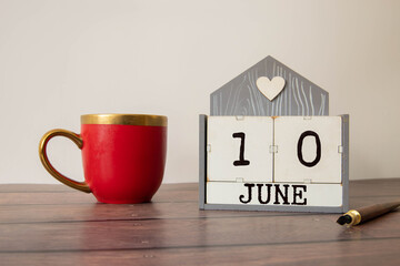 Wooden block calendar with date June 10 on pink concrete background.