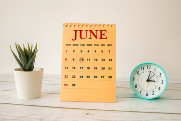 Wooden block calendar with date June 10 on pink concrete background.