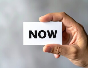 Hand holding card with 'now' text in focus