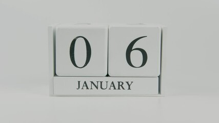 A hand flips a wooden calendar from January 6th to January 7th on a white background, marking the passing of time and the start of a new day
