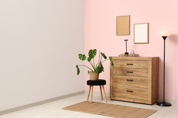 Wooden chest of drawers with lamps and houseplant near pink wall in room