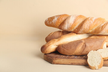 Wooden board with fresh baguettes on beige background