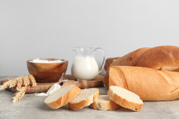 Fresh baguettes with flour and jug of milk on grey background