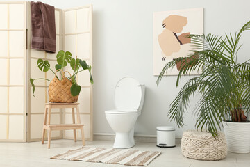 Interior of restroom with folding screen, toilet bowl and palm plants