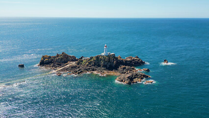 Panoramic scenic aerial drone view of La Corbiere lighthouse on a rocky island surrounded by turquoise water. Jersey, Channel Islands