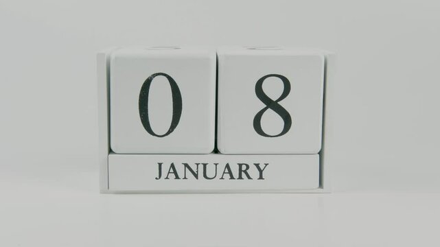 A hand flips a wooden calendar from January 8th to January 9th on a white background, marking the passing of time and the start of a new day