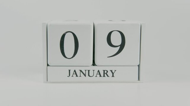 A hand flips a wooden calendar from January 9th to January 10th on a white background, marking the passing of time and the start of a new day