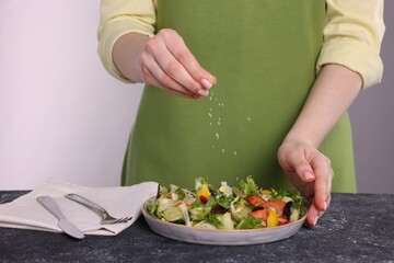 Woman salting tasty salad at dark textured table against white background, closeup