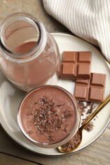 Tasty chocolate milk with shavings and pieces on wooden table, top view