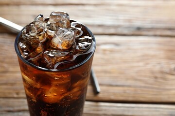 Refreshing cola with ice cubes in glass on wooden table, closeup. Space for text