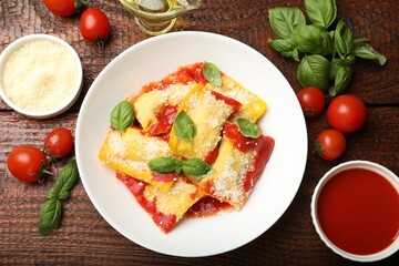 Delicious ravioli with tomato sauce, parmesan cheese and basil on wooden table, flat lay