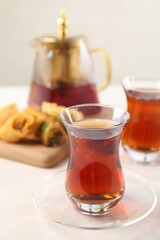 Traditional Turkish tea in glass cups, teapot and fresh baklava on white table, closeup