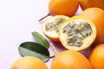 Ripe yellow passion fruits and leaves on lilac background, closeup. Space for text