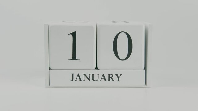 A hand flips a wooden calendar from January 10th to January 11th on a white background, marking the passing of time and the start of a new day