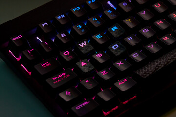 Close-up of a colorful RGB mechanical gaming keyboard illuminated in vibrant hues. Modern computer accessory designed for gaming setups, featuring customizable backlighting and sleek design. 