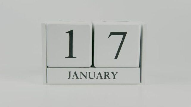 A hand flips a wooden calendar from January 17th to January 18th on a white background, marking the passing of time and the start of a new day