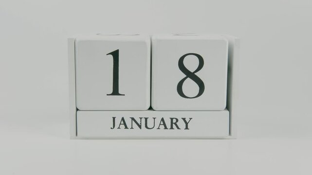 A hand flips a wooden calendar from January 18th to January 19th on a white background, marking the passing of time and the start of a new day
