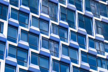 Close-up of blue glass facade with three-dimensional repetitive window modules, highlighting texture, rhythm and depth in modern architectural geometry.