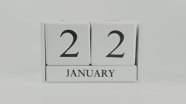 A hand flips a wooden calendar from January 22nd to January 23rd on a white background, marking the passing of time and the start of a new day