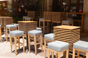 Modern Bar Terrace with High Stools. Stylish outdoor bar area with wooden high tables and patterned stools along a sunny Zakynthos street.