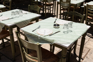 Outdoor Taverna Table Setting. Traditional Greek taverna table set with plates and glassware, shaded and ready for guests in Zakynthos, Greece.