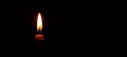 A bright yellow flame dances atop a burning wax candle in the darkness of night