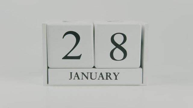 A hand flips a wooden calendar from January 28th to January 29th on a white background, marking the passing of time and the start of a new day