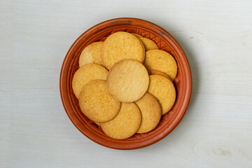 Crispy and spicy biscuits arranged on a clay plate, set against a light wooden surface. These...