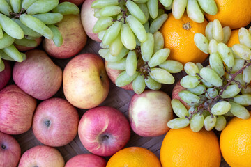 A background of mixed fruits, featuring delicious apples, sweet oranges (or Malta fruit), and green grapes, symbolizing a healthy diet concept.