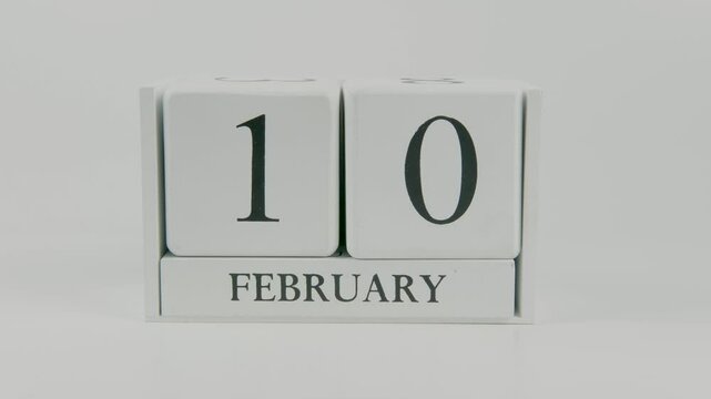 A hand flips a wooden calendar from February 10th to February 11th on a white background, marking the passing of time and the start of a new day