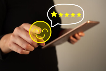 Woman holding a tablet while pointing at an icon of a satisfied face with 5 stars, evaluation...