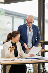 Two business people, a business man and a business woman, engage in a discussion as they read a financial report together. asian business professionals working together in a modern finance company.