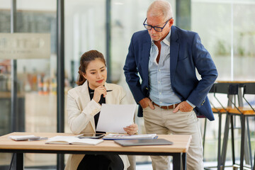 Two business people, a business man and a business woman, engage in a discussion as they read a financial report together. asian business professionals working together in a modern finance company.
