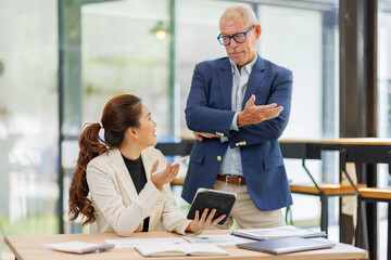 Two business people, a business man and a business woman, engage in a discussion as they read a financial report together. asian business professionals working together in a modern finance company.