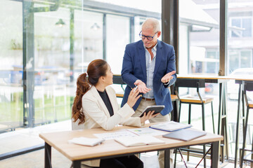 Two business people, a business man and a business woman, engage in a discussion as they read a financial report together. asian business professionals working together in a modern finance company.
