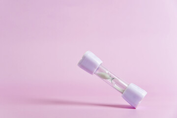 Small white hourglass falling against a soft pink background, symbolizing time passing and the importance of deadlines