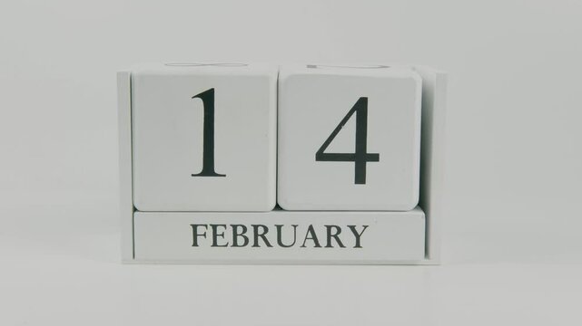 A hand flips a wooden calendar from February 14th to February 15th on a white background, marking the passing of time and the start of a new day