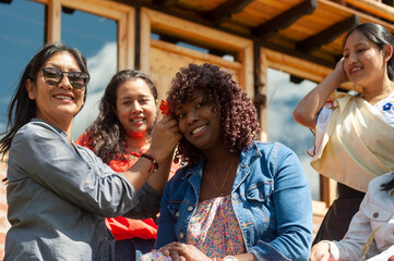 Woman placing flower in friend's hair while smiling outdoors