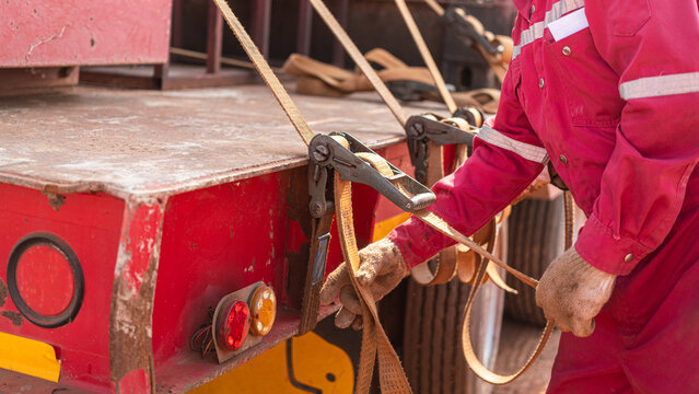 Action of a worker is tightening latching strap belt to secure the load object on trailer truck. Transportation working scene, selective focus.	