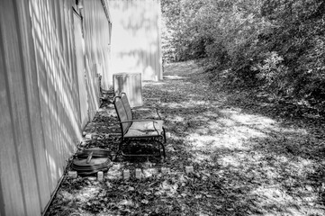 Black and White photo of a bench, somewhere in an area near a building and trees