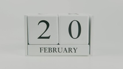 A hand flips a wooden calendar from February 20th to February 21st on a white background, marking the passing of time and the start of a new day