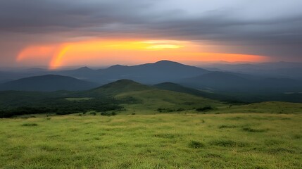 Obraz premium Majestic Mountain Range Sunset Landscape with Double Rainbow Over Grassy Field
