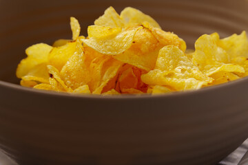 Close-up of crispy potato chips filling a brown bowl, ready to be enjoyed as a savory snack