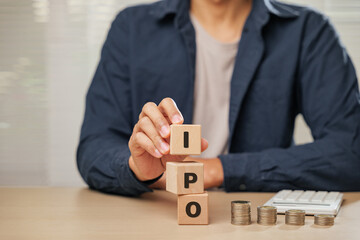 Close up businessman hand holding wooden cube blocks spelling IPO near coins and a calculator....