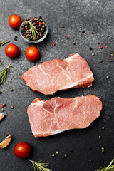 Fresh raw pork chops with spices and vegetables on dark stone background