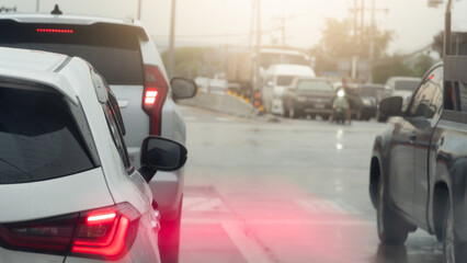 Rear side of white car driving on the road. Motion of tail light of car.Traffic in the rainy time. Road with wet water of rain. Background of junction with many car stop by traffic light control.