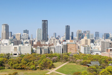 Obraz premium Osaka, Japan - April 14, 2024: The Osaka skyline, featuring modern glass skyscrapers, as seen from the top of Osaka Castle in the park in Osaka Castle, with a clear blue sky in the background.
